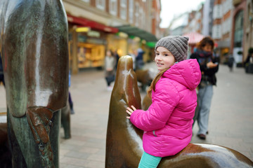 Cute little tourist sitting on popular sculpture of pig family, swineherd and his dog in Bremen
