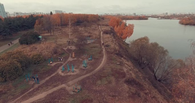 Aerial shot of golden trees on river bank during autumn season. People walking along the footpath near river bank. Moscow suburbs, Strogino district, Russia.