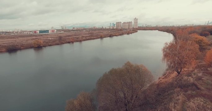 Aerial shot of golden trees on river bank during autumn season. People walking along the footpath near river bank. Moscow suburbs, Strogino district, Russia.