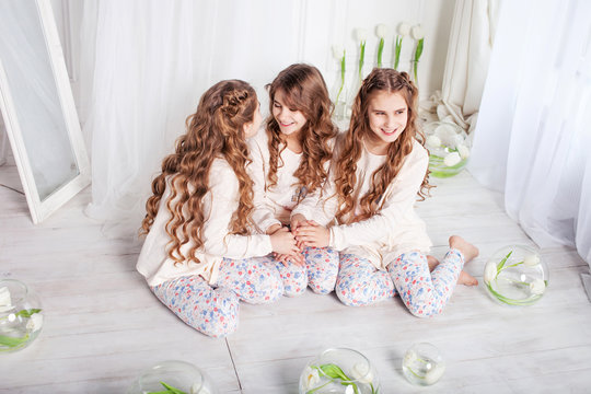 Three pretty little girls sit on a floorand whisper each other