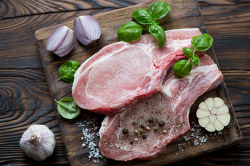 Raw seasoned pork meat steaks on bone in a rustic wooden setting