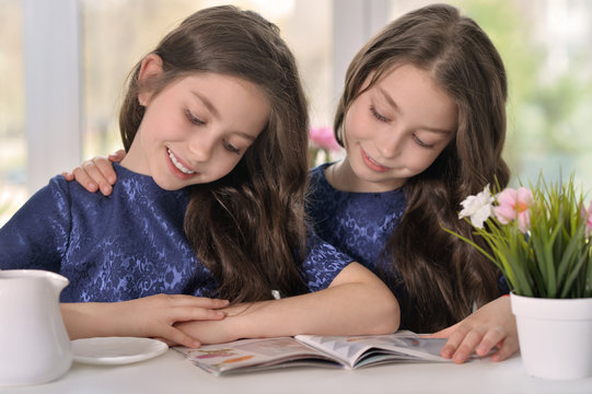 Little Twin Girls Reading A Magazine