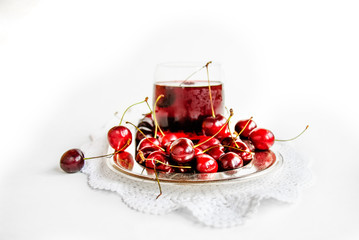 Tasty fresh cherry and cherry juice on metal plate with laced napkin, on white background, selective focus (closeup)