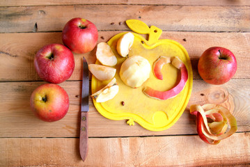 Peeling, deseeding and slicing apples, apple-shaped cutting board, on weathered wooden background