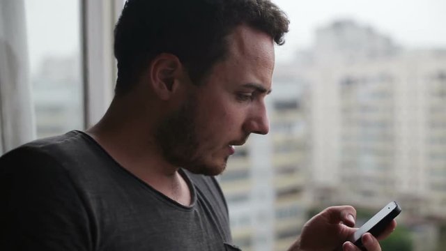 Young man drinking coffee and using smartphone on balcony