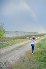 Fototapeta na wymiar The girl swung her hands to the rainbow in the sky, back along the dirt road, full length.
