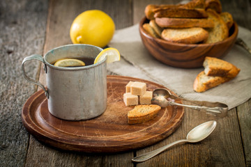 metal cup of tea, brown sugar, crackers and lemon