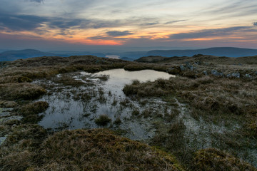 Vibrant orange sunrise with boggy water from Place Fell in the English Lake District.