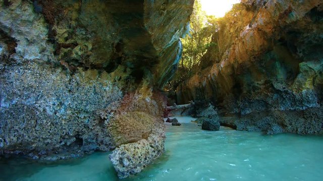 Eroded, natural fissure in a limestone seacliff reveals a tiny, hidden, sandy, tropical beach. Video UltraHD