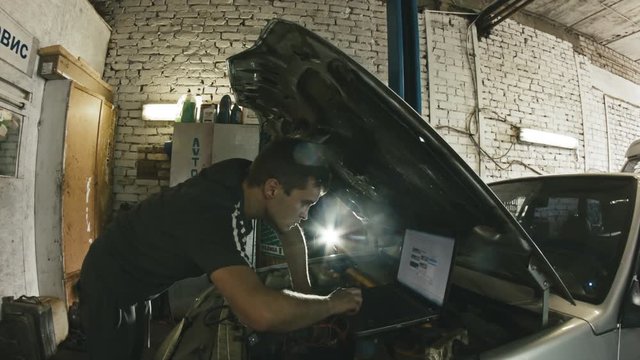 Car service, computer diagnostics: mechanic repairs the damage using the pc