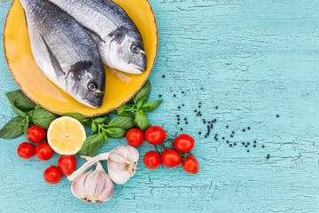 Fresh dorado fish on yellow plate with tomatoes on blue table. Top view, copy space.