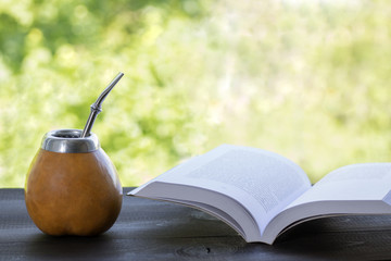 yerba mate in gourd matero with open book on wooden table