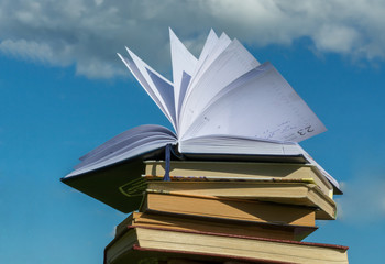 Opened notebook is on the stack of books over blue sky