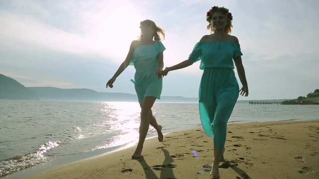 Silhouette of two young women running around and jumping on the sandy beach at sunset. Friendship, summer vacation, holidays, party and people concept - group of smiling teen girls jumping on beach.