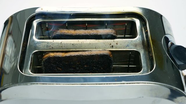 Two burnt slices of bread coming out of a toaster