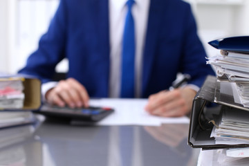 Binders with papers are waiting to be processed with businessman back in blur. Accounting planning budget, audit, insurance  and business concept