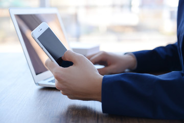 Man using laptop and smart phone at the table in office against the window