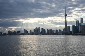 TORONTO SKYLINE WITH SUNBEAMS AND AIRPLANE IN THE DISTANCE