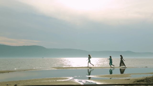 Party and people concept - group of smiling teen girls jumping on beach. Silhouette of three young women running around and jumping on the sandy beach at sunset.