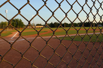 A wide angle shot of a baseball field shot through a chain-link fence at dusk..