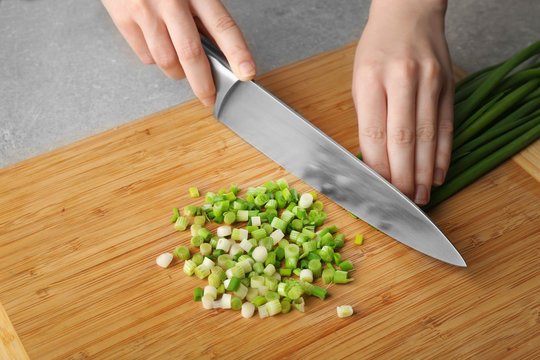 Hands chopping fresh green onion on wooden cutting board