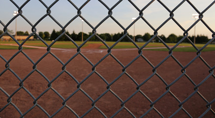 A wide angle shot of a baseball field shot through a chain-link fence at dusk..
