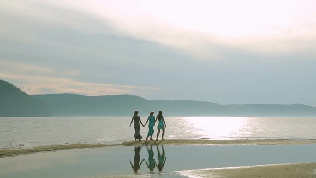 Party and people concept - group of smiling teen girls jumping on beach. Silhouette of three young women running around and jumping on the sandy beach at sunset.
