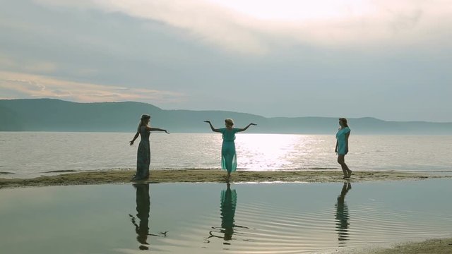 Party and people concept - group of smiling teen girls jumping on beach. Silhouette of three young women running around and jumping on the sandy beach at sunset.