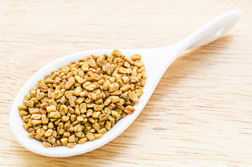 fenugreek seeds in white spoon.