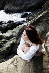 Latina Woman Sitting On Rocks At Sea Shore Looking Out