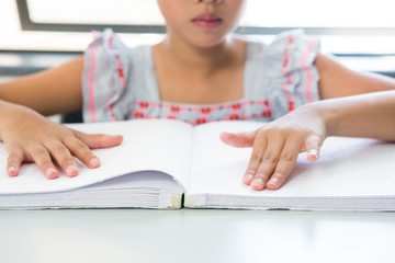 Midsection of blind girl reading braille book