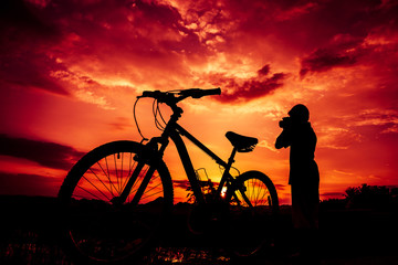 Silhouette of boy and bicycle on sunset background