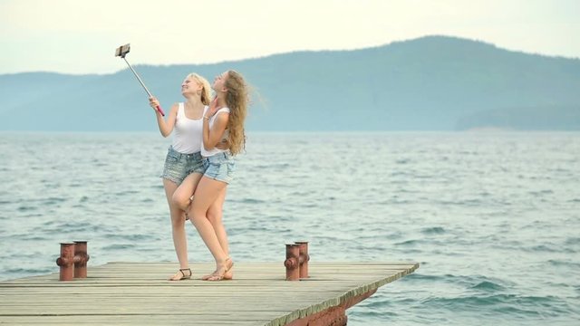 Two friends women taking selfie with mobile phone near the river. Two young girls enjoying near river and taking selfie using smart phone.