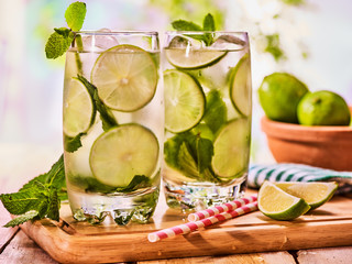 Alcohol drink. On wooden boards two glasses with alcohol drink and ice cubes. A drink number thirty three cocktail mohito with straw and lime and mint leaf. Country life. Outdoor. Light background.