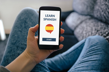 Hand holding smart phone with online learn spanish concept on screen. All screen content is...
