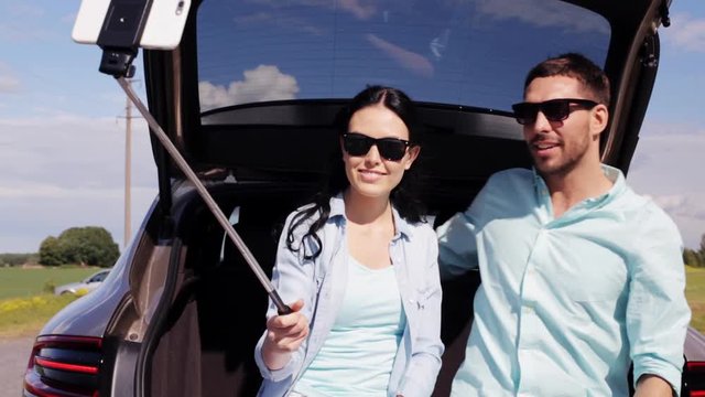 couple with smartphone selfie stick at car trunk 12