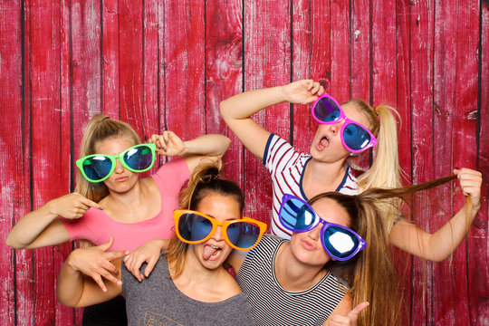 Mädchengruppe mit Brillen albern vor einer Fotobox - freche Mädchen mit Sonnenbrillen 
