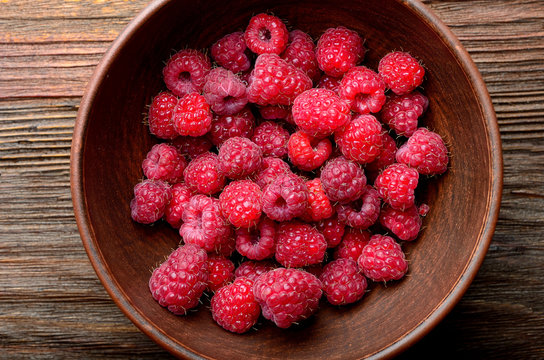 raspberries in a clay bowl on a wooden table