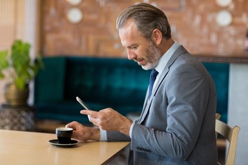 Businessman using mobile phone while having a cup of tea