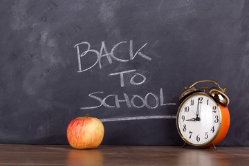 Clock and an apple against a blackboard