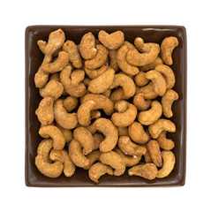 Whole honey roasted cashews in a square dish top view isolated on a white background.