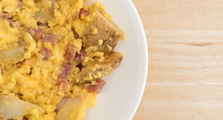 Ham eggs and potatoes breakfast TV dinner on a plate atop a wood table.