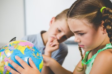 School kids looking at globe in classroom