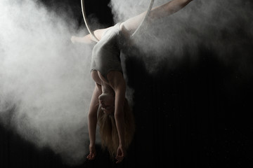 Acrobatic woman doing gymnastic cross twine on aerial hoop with flour