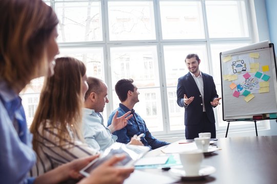 Coworkers Looking At Smiling Businessman Giving Presentation