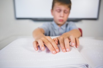 Schoolboy reading a braille book in classroom
