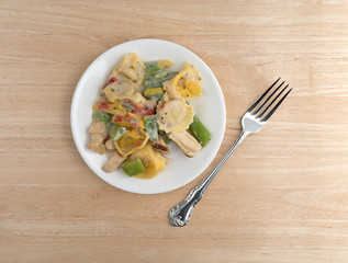 Chicken and tortellini TV dinner on plate with a fork to the side atop a wood table.