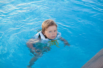 Cute little child swimming with life jacket in outdoor pool
