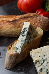 Blue cheese with french baguette, tomato and herbs on black marble table. Traditional snacks in France and Italy.