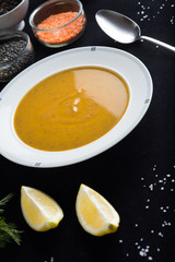 Cream soup of assorted lentil. Yellow and green lens, spices as raw for meal and lemon on black background. Healthy, appetizing, delicious, vegetarian food. Top view, copy space.
